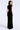 A woman modeling a sleeveless black velvet maxi dress from the back, shown against a plain light gray studio background.