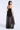 A model shown from the back wearing a strapless black tulle dress with a sheer overlay and a wide black waistband, photographed against a light gray studio background.
