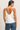 A woman shown from the back wearing a white satin camisole top with thin straps and a deep V-back, paired with blue jeans, against a plain light background.