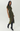 A woman models a short-sleeved olive green midi dress with a black floral jacquard pattern, featuring a high side slit and black knee-high heeled boots, against a plain light gray studio background.