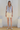 Woman wearing a tie-dye top and light-colored shorts in a minimal indoor setting.