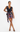 A woman modeling a sleeveless black wrap mini dress with a colorful floral print and a cowl neckline, standing against a plain white studio background.