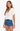 Woman wearing a white crochet top and denim shorts on a white background
