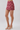 A model's lower body wearing a high-waisted, short A-line mini skirt with a pink and red paisley pattern, paired with metallic gold heeled sandals against a light gray studio background.
