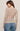 Woman wearing a beige patterned sweater and blue jeans on a plain background