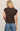 Woman wearing a brown sleeveless top with decorative straps on a beige background