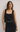 Woman wearing a black sleeveless top with scalloped edge design against a plain background