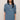A woman modeling a medium-wash blue denim shirt dress with three-quarter sleeves, a buttoned collar, and two chest pockets, set against a plain beige background.