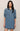 A woman modeling a medium-wash blue denim shirt dress with three-quarter sleeves, a buttoned collar, and two chest pockets, set against a plain beige background.