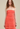 Woman wearing a strapless, ruched coral dress against a beige background