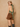 A woman models a green satin halter back top and brown shorts against a textured beige background.