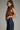 Woman wearing a brown sleeveless top and blue jeans on a gray background