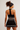 A woman shown from the back wearing a black athletic crop top and matching skirt with white horizontal stripes, along with a black headband, against a plain light background.