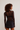 A model shown from the back wearing a sheer black long-sleeve mesh top with a subtle polka dot pattern and a black denim mini skirt, set against a plain light gray studio background.