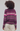 A person shown from the back wearing a fuzzy striped knit sweater with horizontal bands of purple, pink, beige, and gray, paired with cream pants, against a light gray studio background.