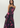 A woman modeling a strapless black maxi dress with a vibrant pink and purple floral print, photographed against a solid light gray studio background.