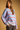 A woman wearing a chunky knit sweater with horizontal stripes in light blue, white, and red, paired with dark gray pants, set against a solid warm tan background.