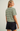 A woman shown from the back wearing a short-sleeve crewneck t-shirt with thin dark green horizontal stripes on an off-white base, paired with dark denim shorts, against a plain light gray studio background.