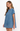 A woman wearing a short-sleeve blue denim dress, shown from a side profile against a plain white studio background.