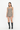 A model stands against a plain white studio background wearing a sleeveless brown, black, and beige gingham mini romper with black knee-high boots.