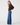 A woman modeling a dark brown knit sweater with a fuzzy collar and wide-leg blue jeans against a plain light gray studio background.