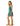 A woman modeling a teal green polka-dot dress with ruffled shoulder straps and a flared hem, paired with tan knee-high boots, against a plain white studio background.