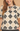 A woman wearing a short-sleeve crochet top with a black and cream geometric pattern and a tie-neck detail, shown against a warm beige background.