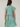 A woman shown from the back wearing a tiered dress with vertical stripes in green, blue, pink, and white on a light beige studio background.