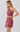 A woman modeling a two-piece matching set featuring a halter crop top with a floral paisley pattern and a high-waisted mini skirt, in a dusty rose pink color, against a light gray studio background.