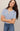 Woman wearing a light blue textured shirt and jeans against a neutral background