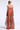 Woman wearing a strapless, long, sheer dress with red and pink abstract pattern on a white background