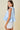 Woman wearing a light blue sleeveless top with ruffled details on a beige background