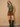 A woman models a green satin halter top and brown drawstring shorts against a textured beige wall, wearing black knee-high leather boots.