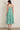 Woman wearing a green and white striped strapless dress against a white tiled wall.