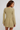 A woman shown from the back wearing a light olive-beige knit long-sleeve mini dress with a scalloped hem, photographed against a plain light gray studio background.