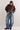 A model wearing a dark brown leather jacket, a brown ribbed knit top, wide-leg distressed blue jeans, and black leather boots, standing against a plain off-white studio background.