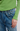 Close-up of a person wearing a lime green ribbed knit top with a scalloped hem and cuffs, paired with blue denim jeans, against a light gray background.