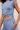 A close-up of a model wearing a light blue sleeveless crop top and matching light blue sweatpants against a plain light background.