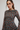 A woman wearing a brown sheer long-sleeve dress with a repeating blue and pink floral pattern, photographed against a plain light gray studio background.