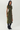 A woman modeling a short-sleeve olive green midi dress with a black floral jacquard pattern, paired with black over-the-knee boots, against a plain light gray studio background.