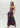 A woman modeling a strapless black maxi dress with a vibrant pink and purple floral print, paired with black high heels, against a plain light gray studio background.