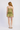 A woman viewed from behind wearing a light olive green ruffled camisole and matching ruffled shorts set, paired with beige woven flat shoes, against a plain white studio background.