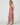 A woman modeling a dusty rose eyelet jumpsuit with a ruffled camisole-style top and wide-leg pants, paired with black flat sandals, against a light gray studio background.