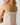 Close-up back view of a woman wearing a cream lace camisole with thin tie straps and a scalloped lace neckline, against a light gray studio background.