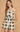 A woman modeling a sleeveless crochet romper with a black and beige geometric pattern, set against a textured beige background.