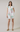 Woman wearing a white dress with floral embroidery on a plain background