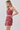 A woman modeling a matching two-piece outfit featuring a halter crop top and high-waisted mini skirt in a dusty rose paisley pattern, set against a plain light gray studio background.