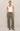 Woman wearing a white tank top and green pants on a beige background