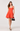 Woman wearing an orange dress holding a black handbag on a white background