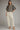 A woman modeling a black and white gingham short-sleeve blouse with puff sleeves and cream wide-leg cropped pants, paired with beige strappy heels, against a solid gray studio background.